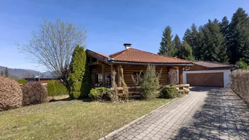 Charmantes Holzhaus im Chalet-Stil mit gepflasterter Auffahrt und Garage, umgeben von Grün.