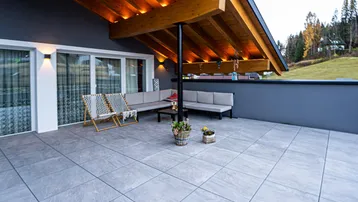 Große überdachte Terrasse mit bequemen Sitzgelegenheiten und Blick ins Grüne.