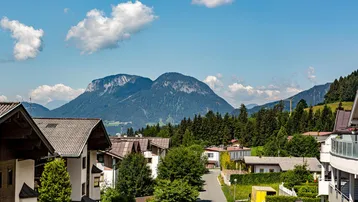 Panoramablick auf eine Berglandschaft mit Häusern und einer Straße unter blauem Himmel.