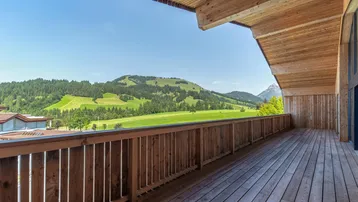 Geräumiger Holzbalkon mit atemberaubendem Blick auf die umliegende grüne Landschaft und die Berge.