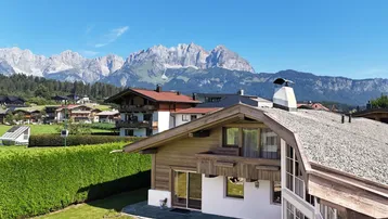 Traditionelles Haus im Alpenstil mit Holzelementen und beeindruckendem Bergblick unter blauem Himmel.