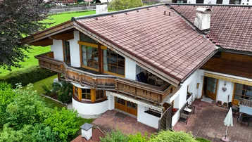 Charmantes Haus mit traditionellen Holzbalkonen und einer gepflasterten Terrasse im Grünen.