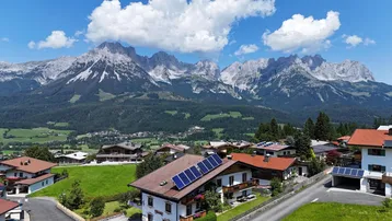 Panoramablick auf ein malerisches Dorf in den Alpen mit grünen Wiesen und majestätischen Bergen im Hintergrund.