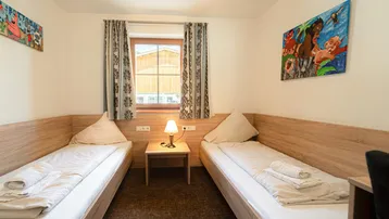Kinderzimmer mit zwei Einzelbetten, bunten Bildern und Blick ins Grüne.