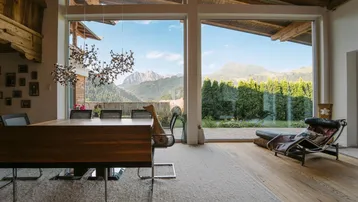 Helles Wohn- und Esszimmer mit Holzbalken, großen Fenstern und atemberaubendem Bergblick.