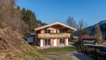 Charmantes Holzchalet mit traditioneller Architektur, umgeben von Natur und Bäumen am Hang.