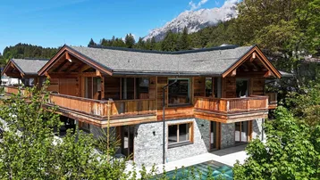 Luxuriöses Holzchalet mit Steinfassade, Balkonen und einem Pool vor alpiner Bergkulisse.