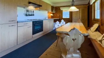 Funktionale Küche mit Holzelementen, Esstisch und Blick auf die grüne Umgebung.