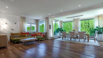 Geräumiger Wohn-Essbereich mit Holzboden, gemütlichem Sofa und Blick ins Grüne durch große Fenster.