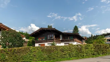 Traditionelles Haus im alpenländischen Stil mit Holzbalkonen und gepflegter Hecke vor dem Grundstück.