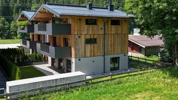 Neubau mit Holzverkleidung, Balkonen und Blick auf die umliegende Berglandschaft.