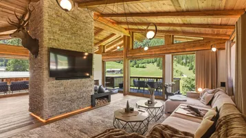 Gemütliches Wohnzimmer im alpinen Stil mit Holzbalkendecke, Kamin und Panoramablick auf die Berge.