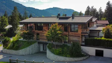 Moderne Holzfassade eines Hauses mit Balkonen und Auffahrt, umgeben von Bergen.