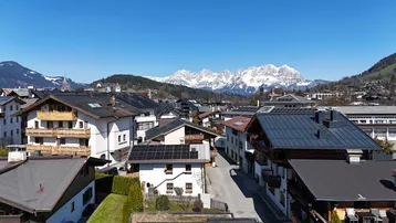 Panoramablick auf eine Siedlung mit traditionellen Häusern und schneebedeckten Bergen im Hintergrund unter blauem Himmel.