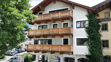 Traditionelles Gebäude mit mehreren Holzbalkonen und Satteldach, umgeben von Bäumen.