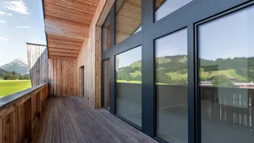 Geräumiger Holzbalkon mit großen Glasfronten und weitem Blick auf die umliegende Berglandschaft.