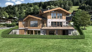 Luxuriöses Chalet mit Holz- und Steinfassade, umgeben von grüner Landschaft und Bergen.