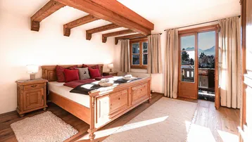 Gemütliches Schlafzimmer mit sichtbaren Holzbalken, Holzboden und direktem Zugang zum Balkon mit Bergblick.