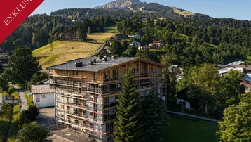 Gebäude im Bau mit Gerüst und beeindruckendem Bergblick in einer grünen Umgebung.