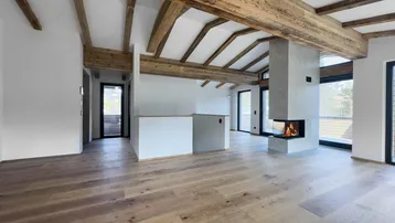 Geräumiges Wohnzimmer mit hohen Decken, sichtbaren Holzbalken und modernem Kamin.