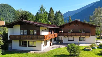Traditionelles Haus im alpenländischen Stil mit Holzbalkonen und Bergblick in sonniger Lage.