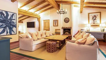 Gemütliches Wohnzimmer mit Kamin, bequemen Sofas und rustikalen Holzbalken an der Decke.