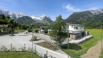 Blick von der Immobilie auf ein modernes Haus mit schneebedeckten Bergen und grünen Wiesen.