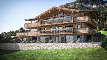 Großes Holzchalet mit mehreren Balkonen und Bergblick in alpiner Umgebung, umgeben von grüner Natur.