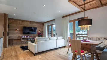 Gemütlicher Wohn- und Essbereich mit Holzwand, großem Esstisch und Zugang zum Balkon mit Bergblick.
