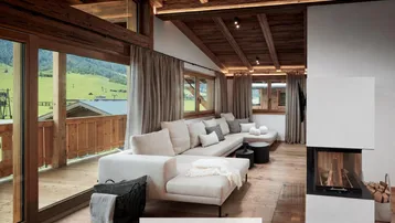 Helles Wohnzimmer mit Kamin, Holzbalkendecke und Zugang zu einem Balkon mit Bergblick.
