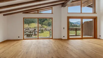 Heller Wohnraum mit Holzbalkendecke, großen Fenstern und Panoramablick auf die Berge und das Tal.