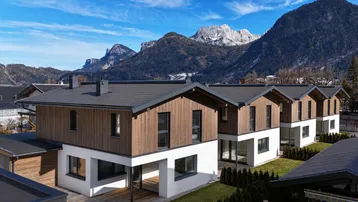 Moderne Reihenhäuser mit Holzfassade und Satteldach vor einer beeindruckenden Bergkulisse.