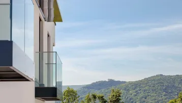Moderner Balkon mit Glasbrüstung und weitem Blick auf die bewaldeten Hügel.