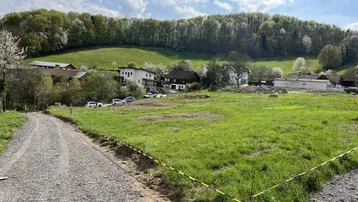 Weitläufiges Grundstück mit Schotterweg und Blick auf die umliegende Hügellandschaft und Häuser.