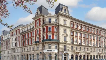 Großes, historisches Gebäude mit eleganter Architektur und blühenden Magnolien im Vordergrund.