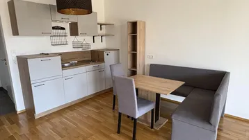 Moderne Küchenzeile mit integriertem Essbereich und hellem Parkettboden in einem offenen Raum.