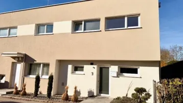 Moderne Gebäudefassade mit beiger und weißer Farbgebung und großen Fenstern.