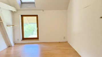 Helles Schlafzimmer mit Holzfußboden, Dachfenster und einem weiteren Fenster mit Blick ins Grüne.