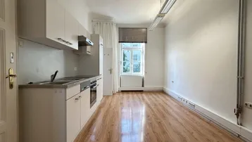 Heller Raum mit integrierter Küchenzeile, Laminatboden und einem Fenster, das Tageslicht hereinlässt.
