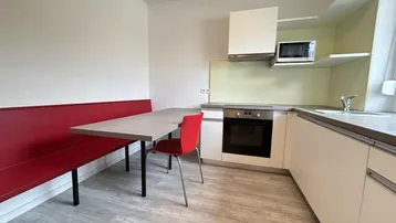 Moderne Einbauküche mit Essbereich, integriertem Backofen und roter Sitzbank.