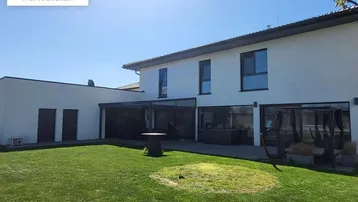Hinteransicht des Hauses mit großem Garten, Rasenfläche und überdachter Terrasse.