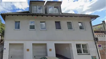 Mehrstöckiges Gebäude mit hellgrauer Fassade, Garagen im Erdgeschoss und Dachgaubenfenstern.
