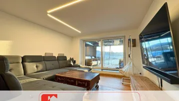 Modernes Wohnzimmer mit bequemer Couch, Holzboden und Zugang zu einem sonnigen Außenbereich.