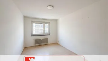 Heller, leerer Raum mit hellem Holzboden, Fenster und Heizkörper, bereit zur individuellen Gestaltung.