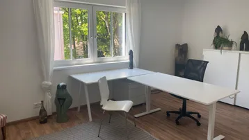 Helles Arbeitszimmer mit zwei Schreibtischen, Laminatboden und einem großen Fenster mit Blick ins Grüne.