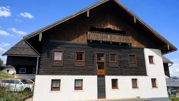 Traditionelles Holzhaus mit weiß getünchter Fassade und Holzbalkon unter blauem Himmel.