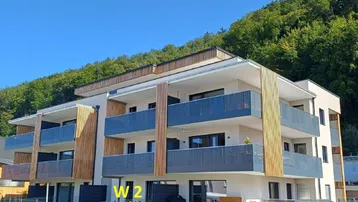 Modernes Mehrfamilienhaus mit mehreren Balkonen, Holzverkleidung und Blick auf die grüne Berglandschaft.