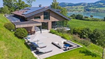 Moderne Villa mit großer Sonnenterrasse, Liegestühlen und atemberaubendem Seeblick.