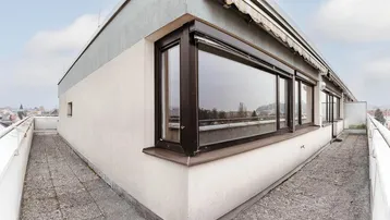 Geräumige Dachterrasse mit Betonplattenboden, großen Fenstern und Markise, ideal für entspannte Stunden mit Fernblick.