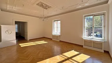 Geräumiges Wohnzimmer mit Fischgrätparkett, Stuckdecke und Kachelofen, durchflutet von Sonnenlicht.